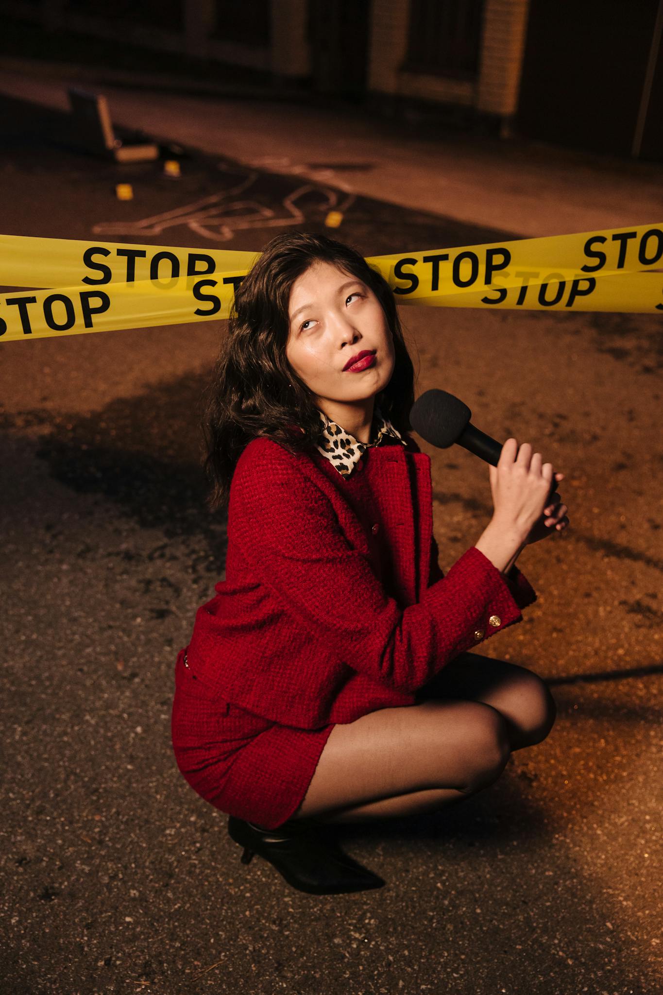 Female reporter poses with microphone behind crime scene tape at night.