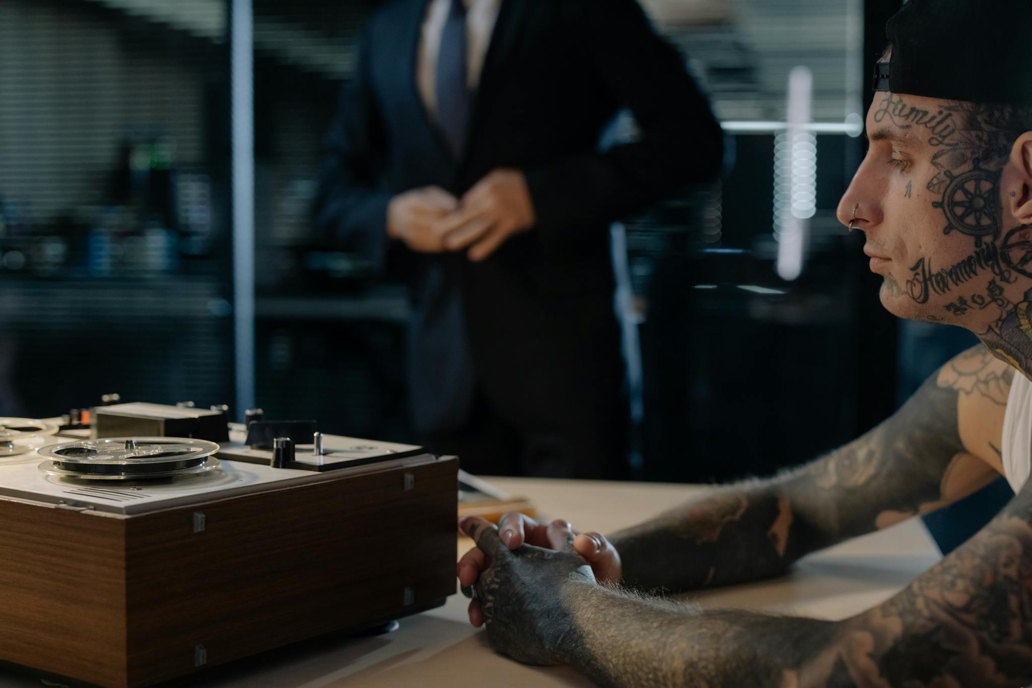 Tattooed man in an investigation room with a vintage recorder, suggesting interrogation or investigation scenario.